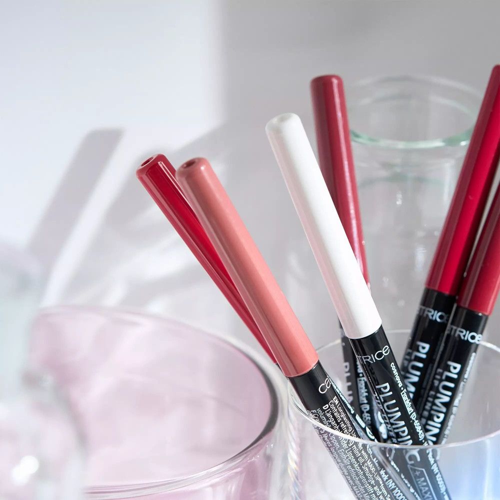 Verschillende lippenpotloden in een glas. Kleuren: rood, roze, wit. Opschrift: PLUMPING + MAXI-LIP. Merk: CATRICE.