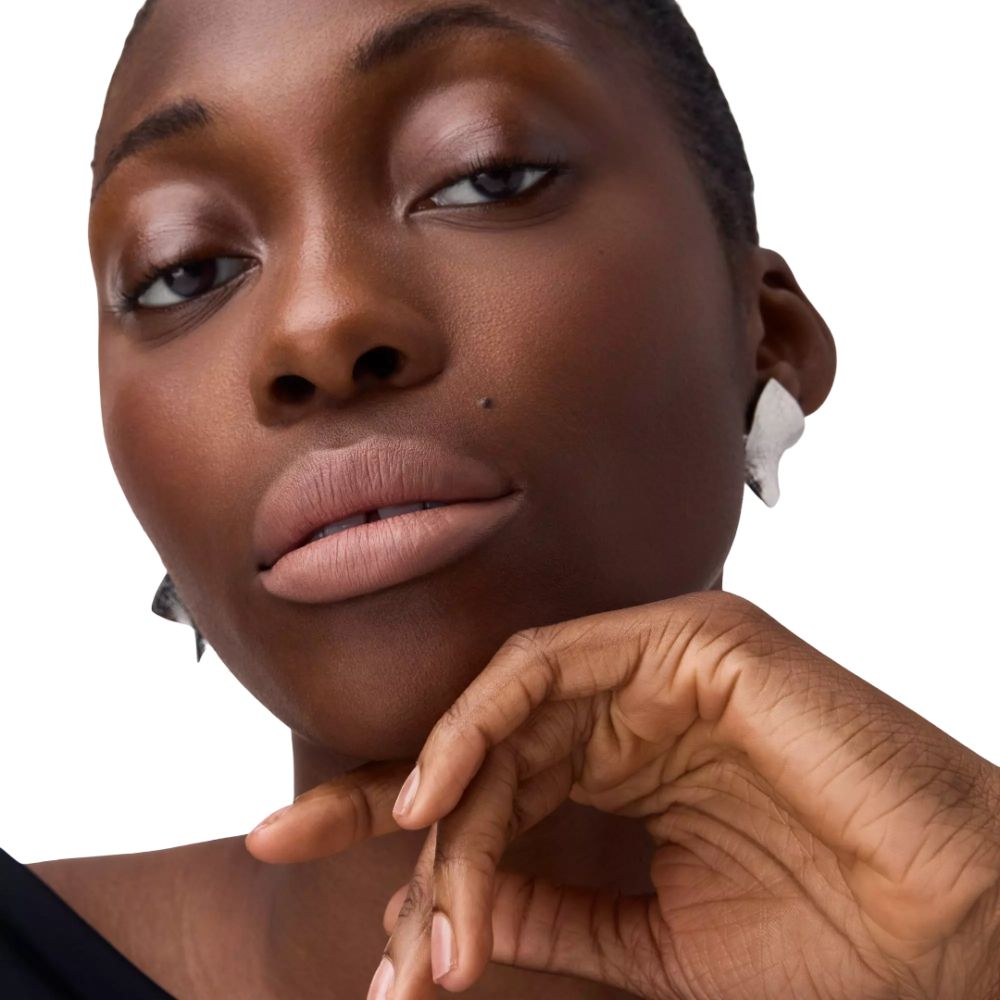 Gros plan d'une femme avec des lèvres brun clair. Elle touche son menton avec sa main.