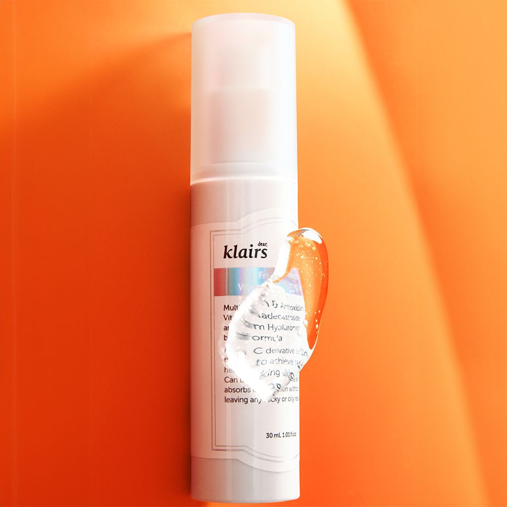 Flacon de sérum blanc avec pompe. Goutte de sérum sur le côté. Inscription : klairs. Fond orange.