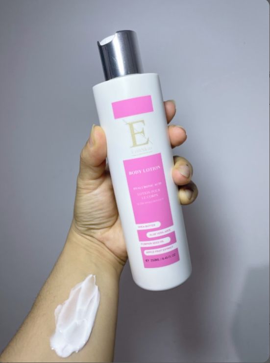 Flacon blanc avec étiquette rose. Bouchon argenté. Main tenant flacon et crème sur le bras. Texte : Body Lotion, Acide hyaluronique + collagène, Aloe vera, Grenade.