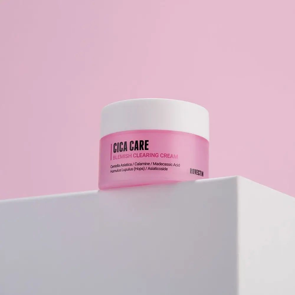 Roze crèmepot met witte deksel. Opschrift: Cica Care Blemish Clearing Cream. Merk: Rovectin. Op witte ondergrond, roze achtergrond.