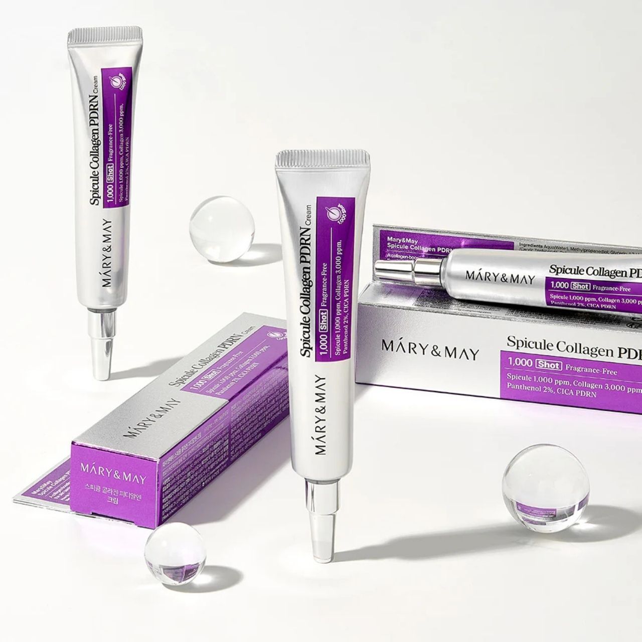 Plusieurs tubes et cartons de Mary&May Spicule Collagen PDRN Cream avec des sphères en verre.