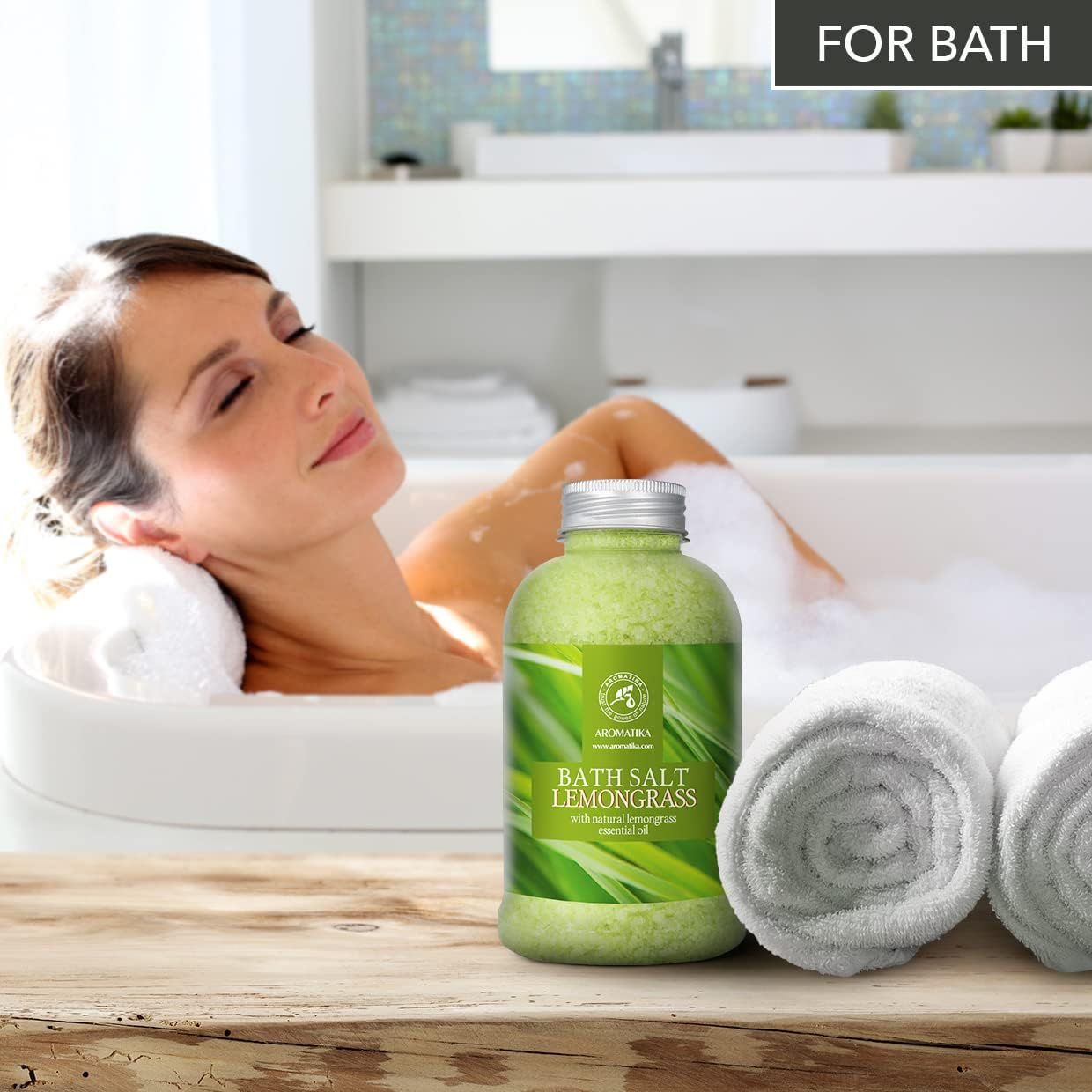 Femme se détendant dans une baignoire moussante à côté d'AROMATIKA Sel de bain Lemongrass. Deux serviettes à côté.