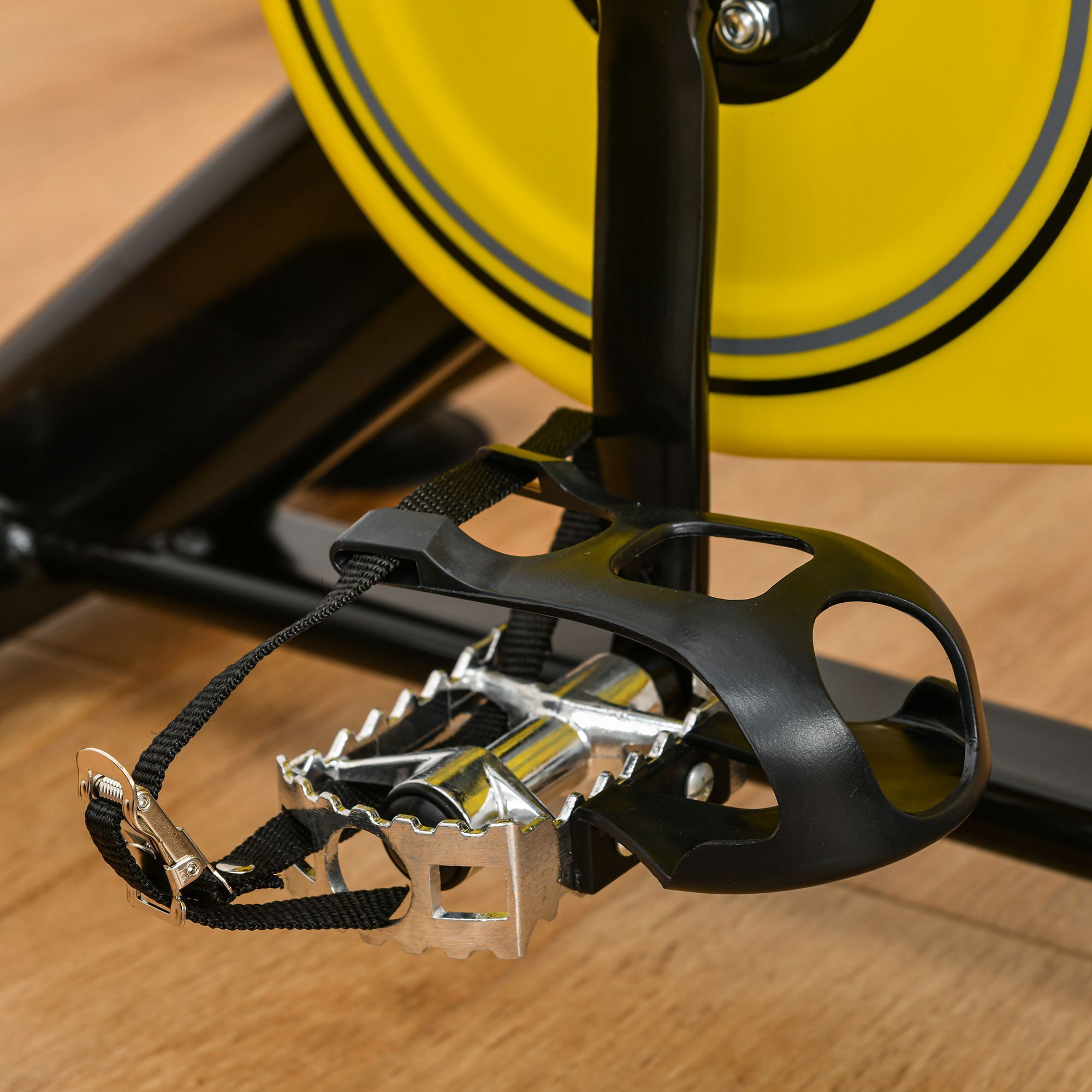 Fietspedaal met zwarte riem. Zwart plastic, zilver metaal. Gele wiel op de achtergrond.