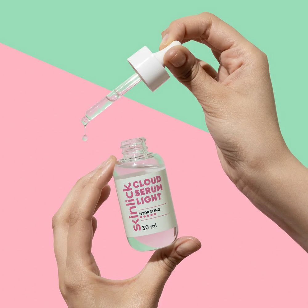 Een hand houdt een glazen flesje van 30 ml "Cloud Serum Light" vast met een pipetapplicator waaruit druppels vallen.