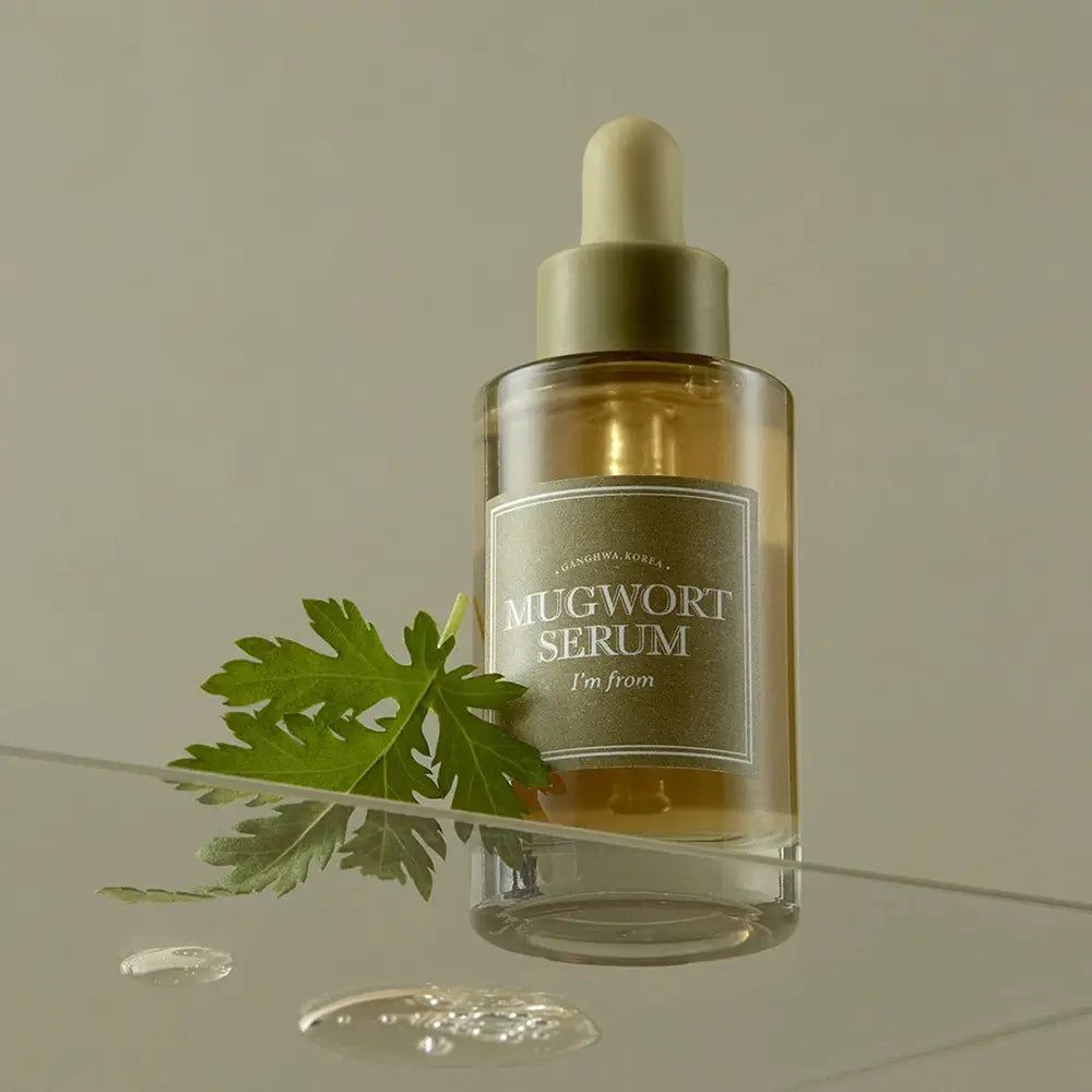 Glazen flesje met serum "Mugwort Serum". Groen blad ernaast. Druppels op glazen oppervlak.