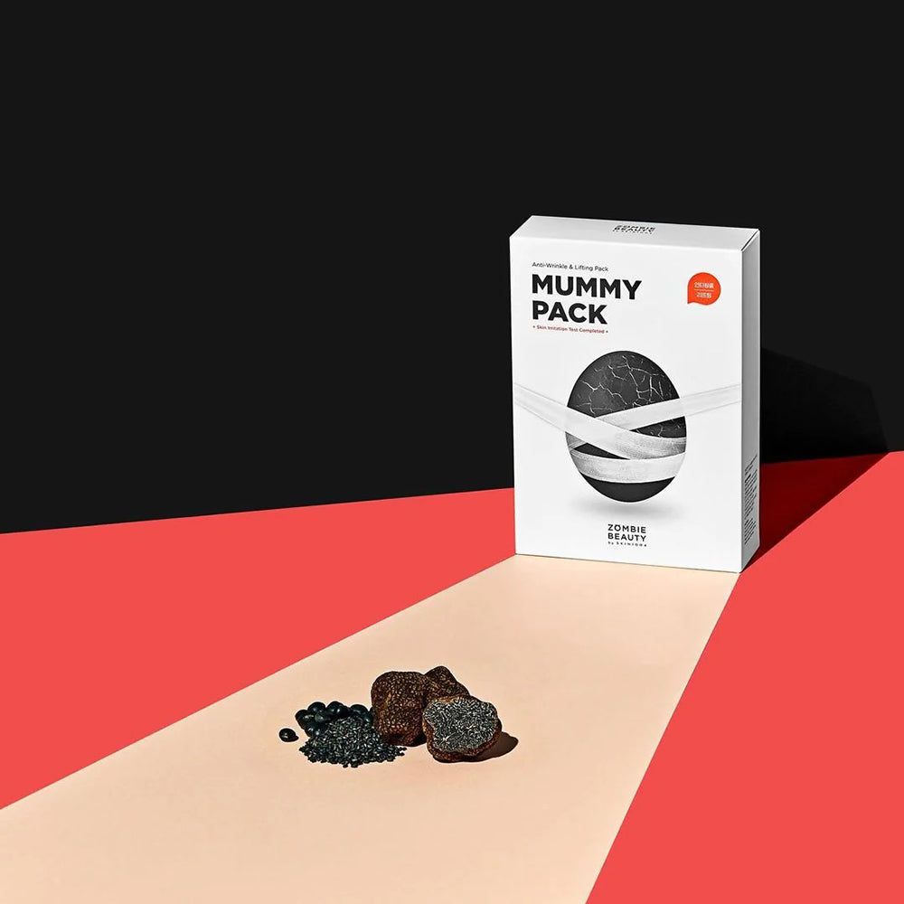 Emballage blanc avec texte "Mummy Pack". Masque noir avec bandes blanches. Accents noirs et rouges. Marque : ZOMBIE BEAUTY.