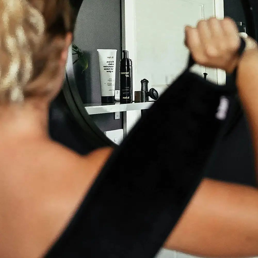 Persoon houdt zwarte applicator vast. Achtergrond: spiegel en producten. De applicator is op de rug te zien.