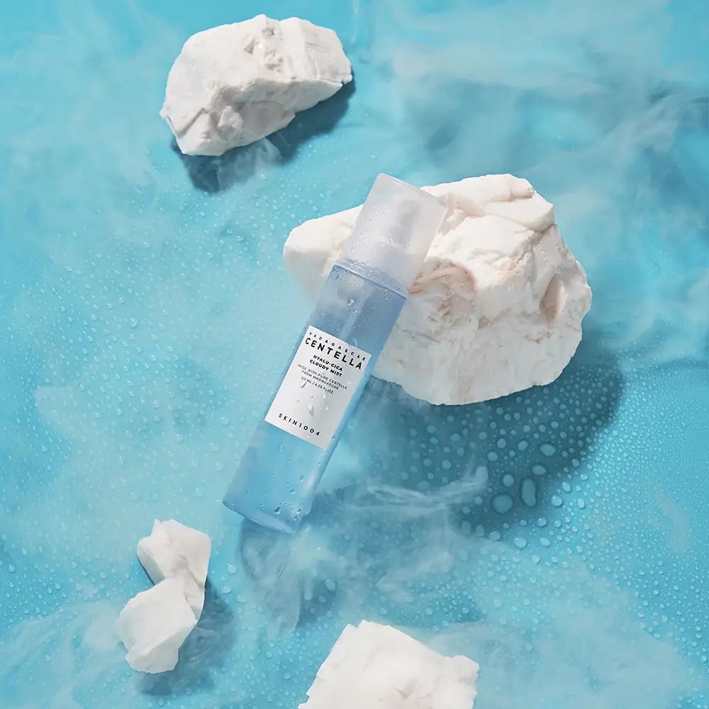 Blauwe mistfles met wit etiket. Op blauwe achtergrond met witte stenen.