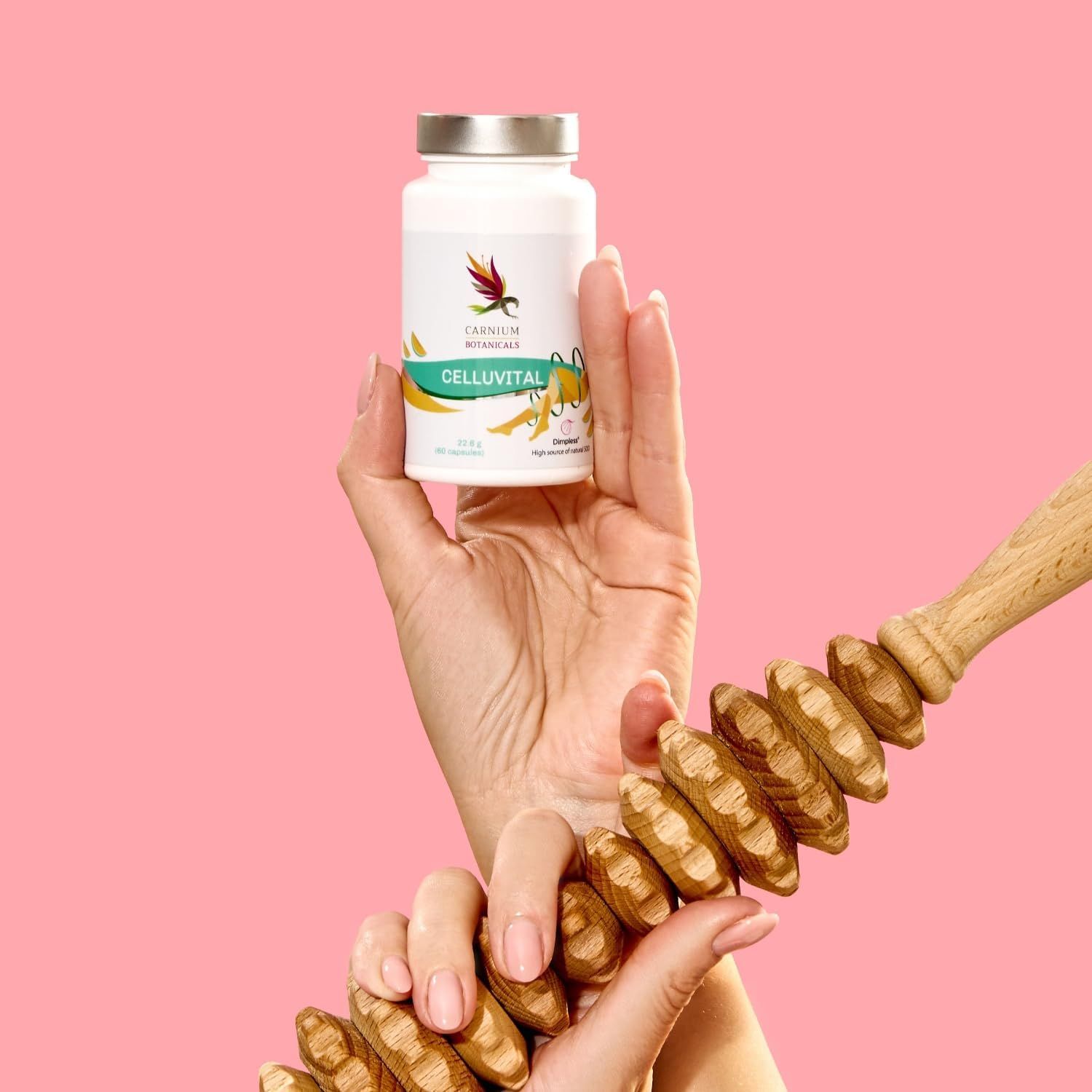 Main tenant un flacon CELLUVITAL et un appareil de massage. Fond rose.