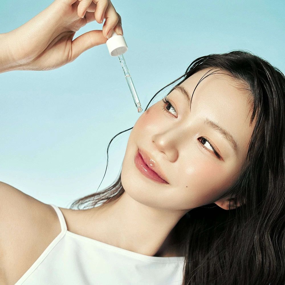 Vrouw met serum applicator. Serum wordt op de wang aangebracht. Blauwe achtergrond.