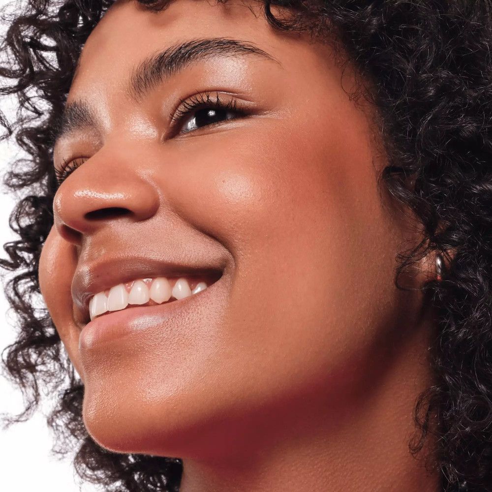 Close-up van een vrouw met een gebruinde huid en blush op de wangen. Ze lacht en heeft krullend haar.