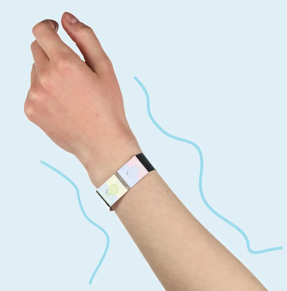 Hand met armband om de pols. De armband heeft meerdere gekleurde testvelden. Blauwe lijnen op de achtergrond.