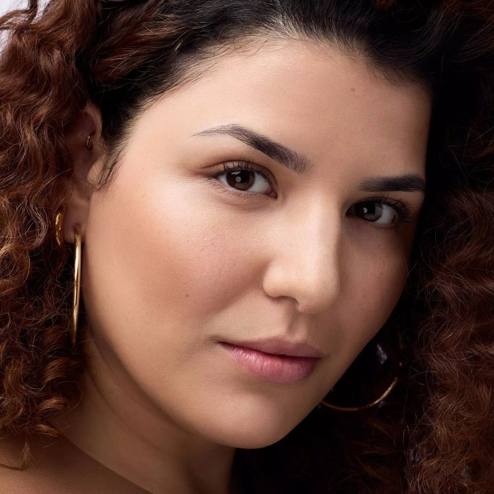 Portrait d'une femme aux cheveux bouclés. Peau bronzée, boucles d'oreilles dorées.