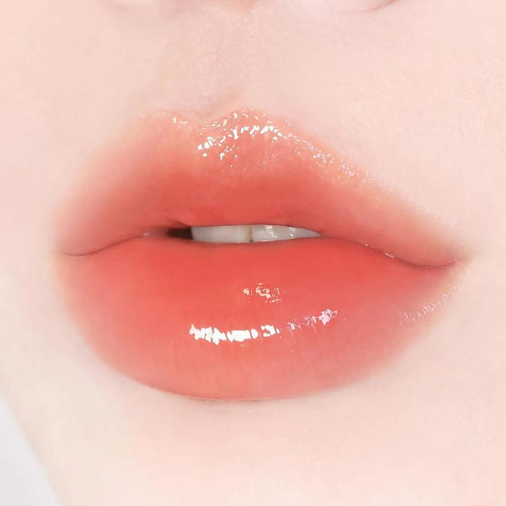 Gros plan sur des lèvres brillantes, avec un baume rose. Les lèvres sont légèrement entrouvertes.