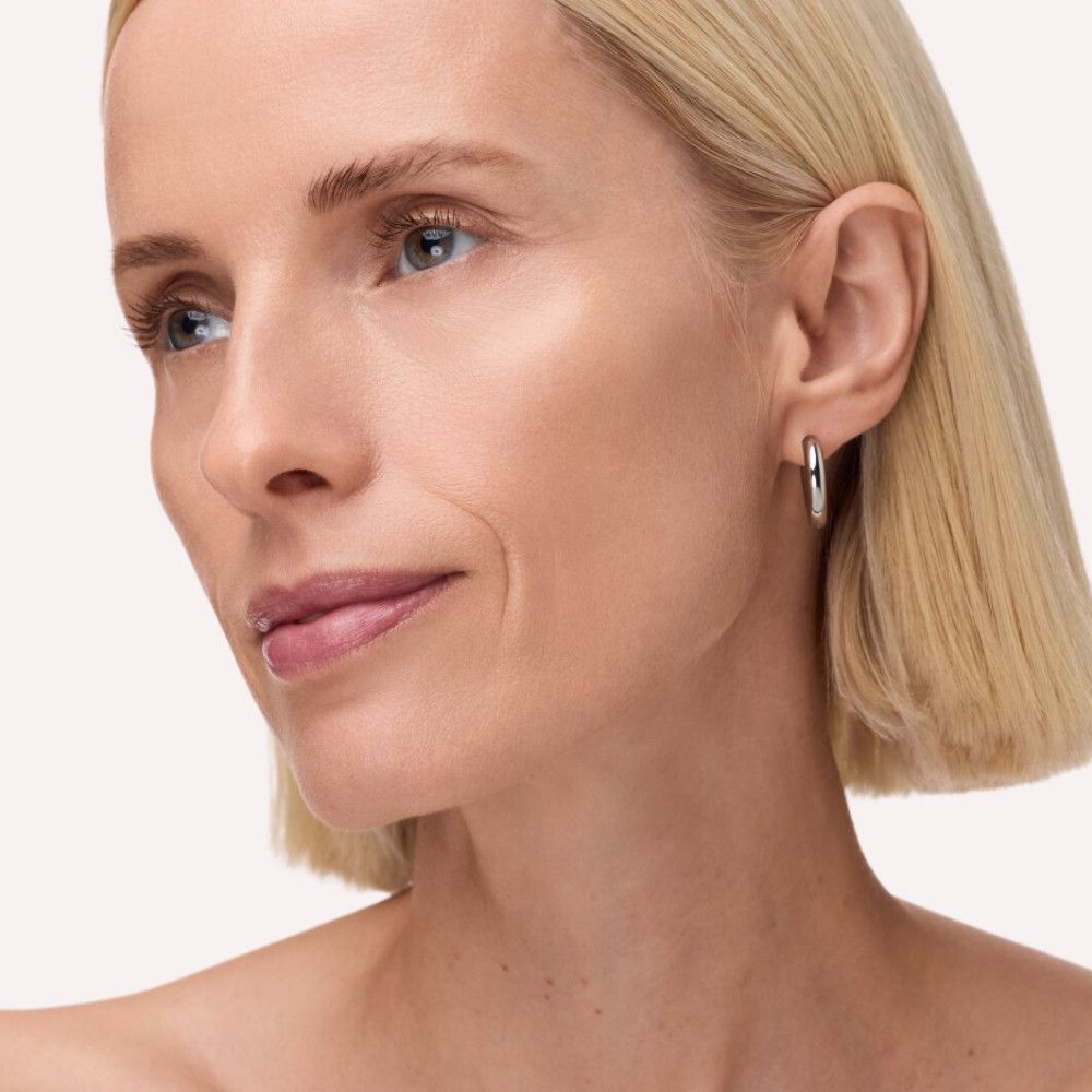 Portrait d'une femme blonde. Elle porte des boucles d'oreilles. Son visage est traité avec un hydratant teinté.