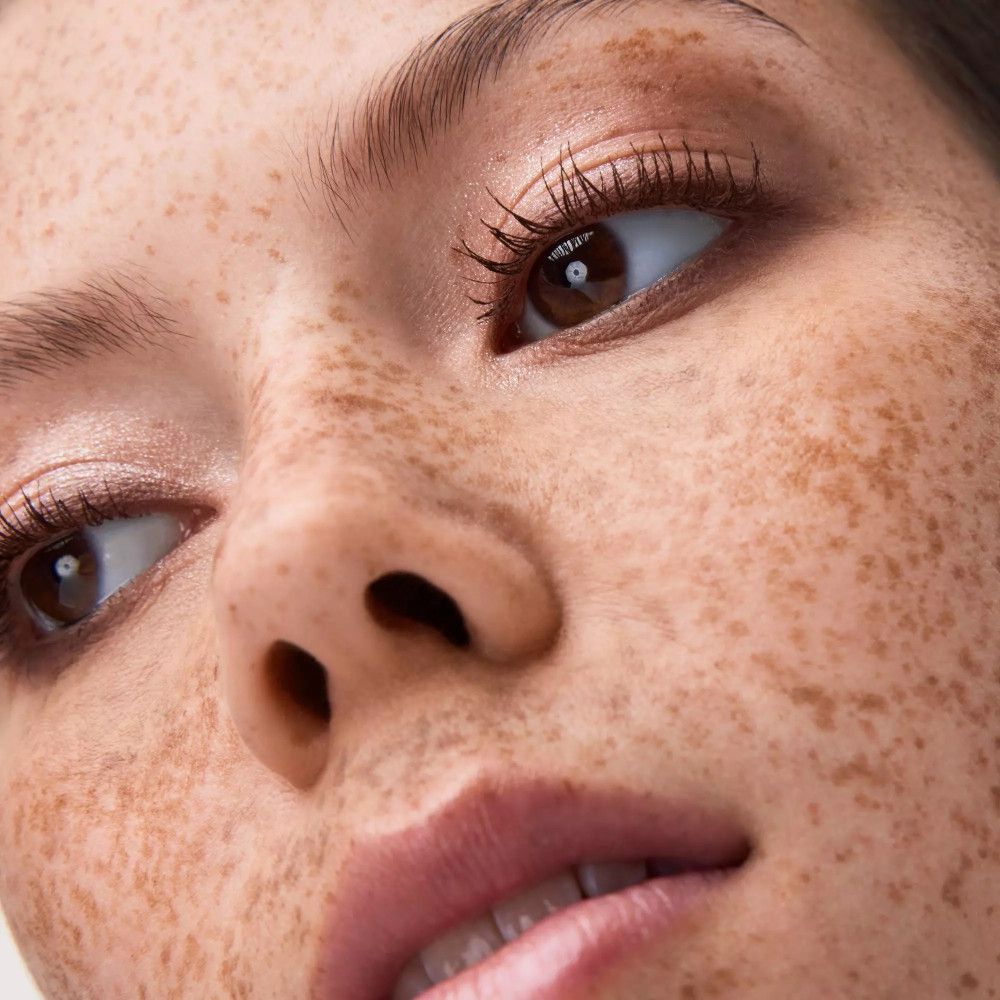 Gros plan d'un visage avec les yeux maquillés. Peau bronzée, taches de rousseur, sourcils et cils foncés.