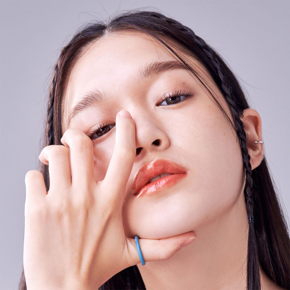 Close-up van een persoon met gevlochten haar. De persoon raakt de lippen aan met de hand, waarop de lippenbalsem is aangebracht.