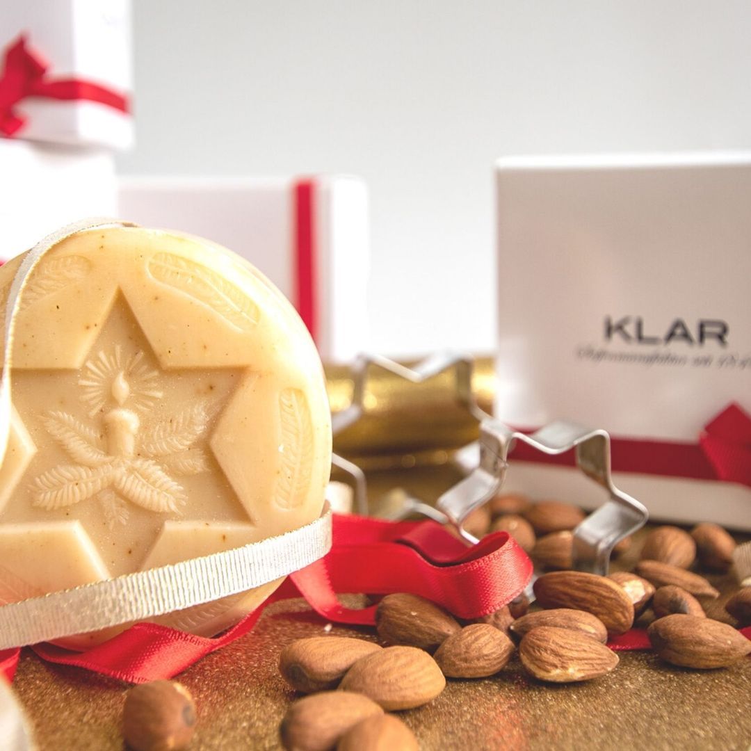 Savon rond avec motif étoile, amandes, emporte-pièce étoile et coffret cadeau avec ruban rouge. Fond doré.