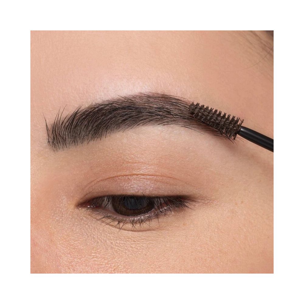 Oog met wenkbrauw die met een borstel wordt bewerkt. De wenkbrauw is donker en vol.