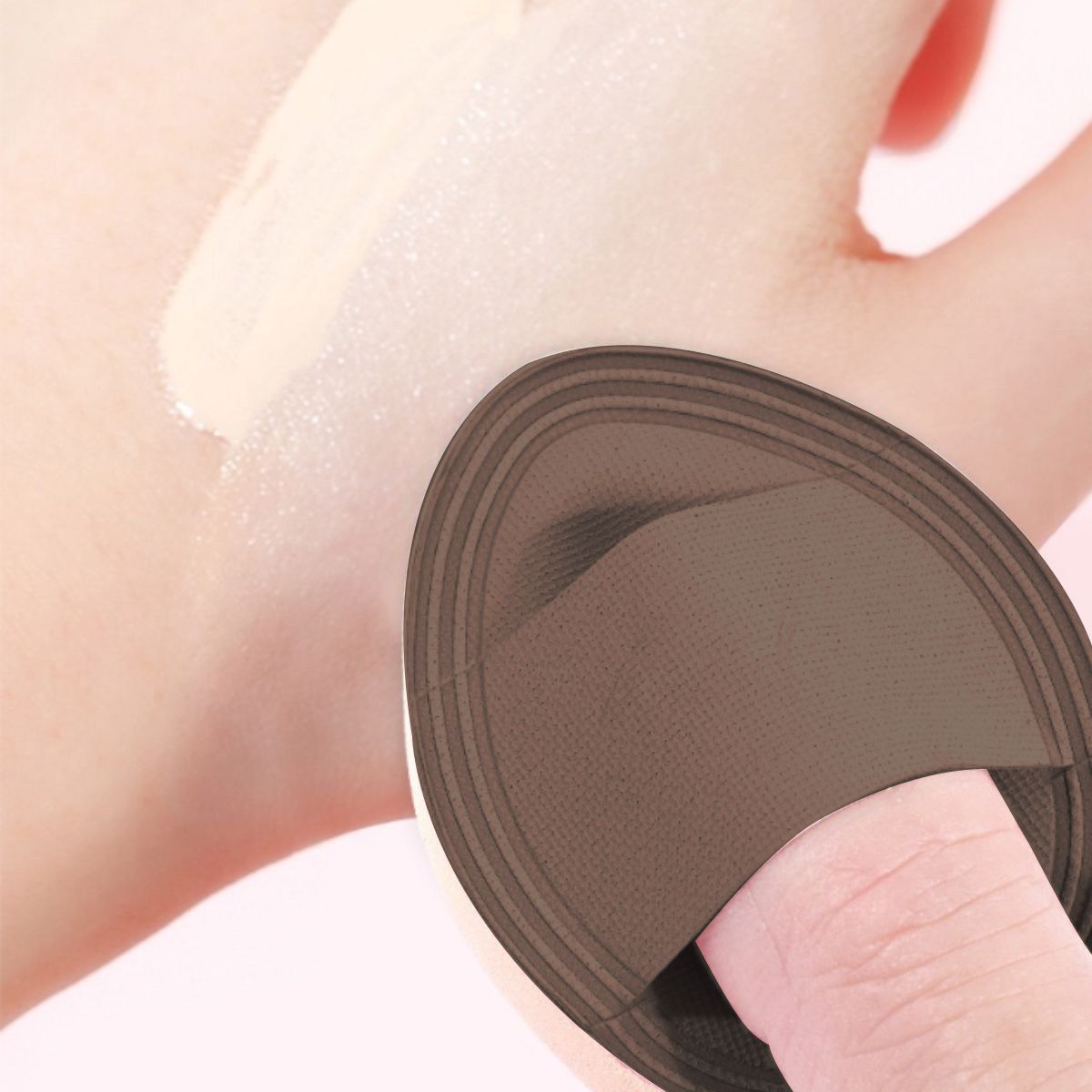 Éponge de maquillage marron avec support pour doigt sur une main avec échantillon de fond de teint.