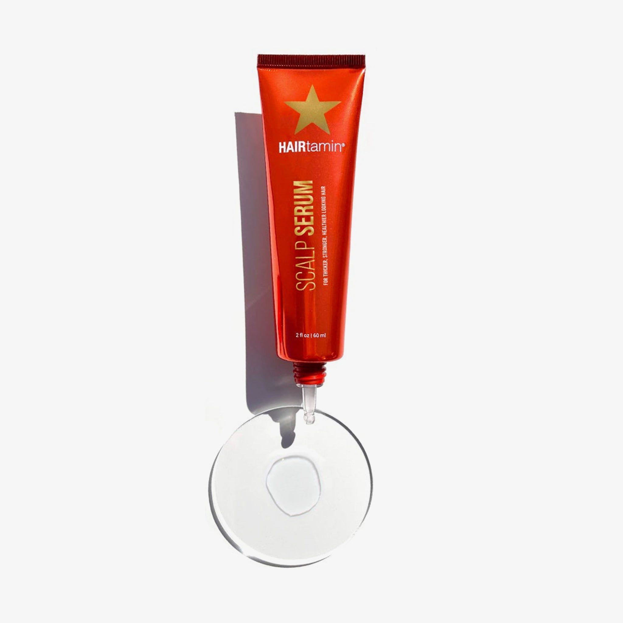 Tube rouge avec sérum sur surface transparente. Nom du produit : Scalp Serum. Marque : HAIRTAMIN.