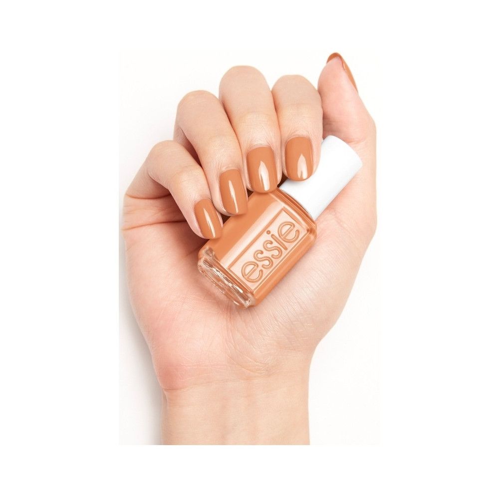 Hand houdt een flesje nagellak vast. De nagels zijn in dezelfde kleur gelakt. Op het flesje staat 'essie'.