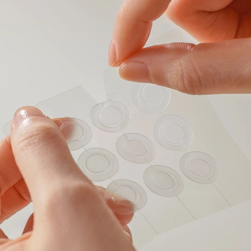 Handen verwijderen transparante, ronde patches van een transparante folie. 10 patches zichtbaar.