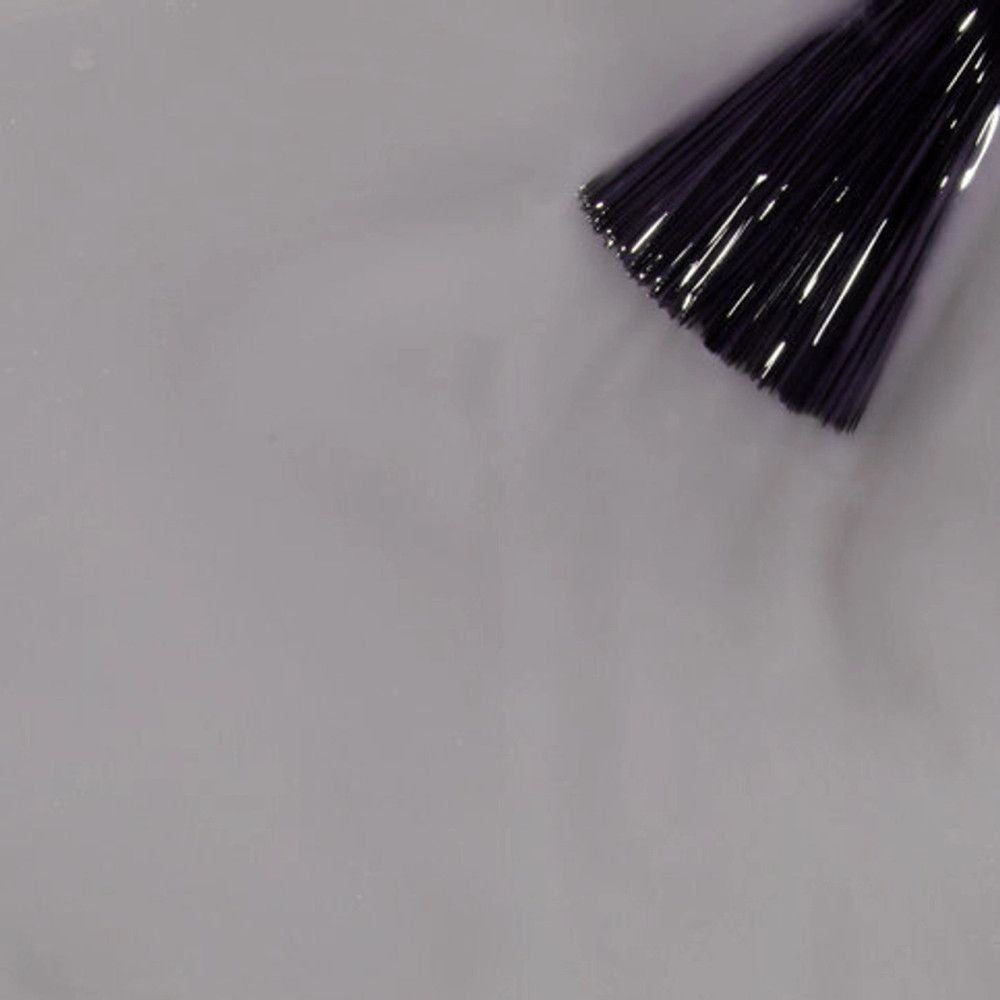 Applicateur de vernis à ongles avec poils sur une surface. Le vernis est gris clair. L'applicateur est foncé.