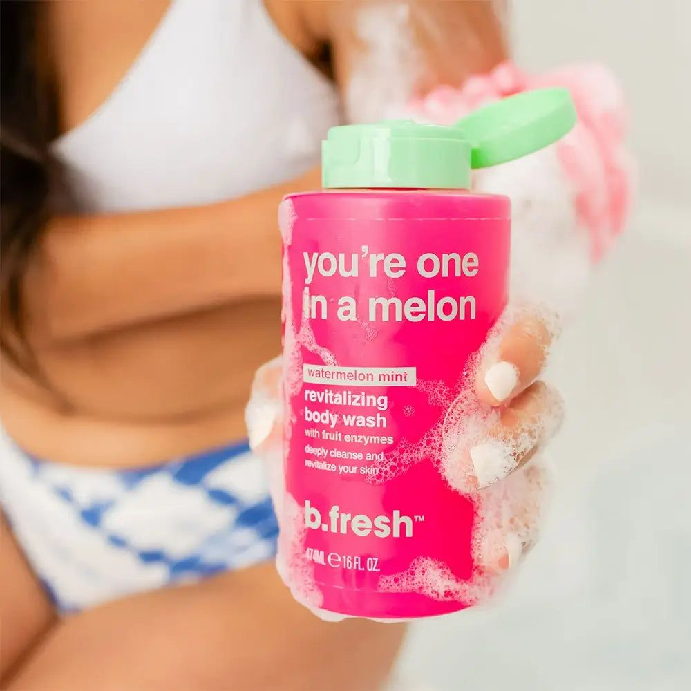 Flacon de gel douche rose avec bouchon vert. Inscription : "you're one in a melon". Nom du produit : b.fresh. La personne tient le flacon et un gant de toilette.