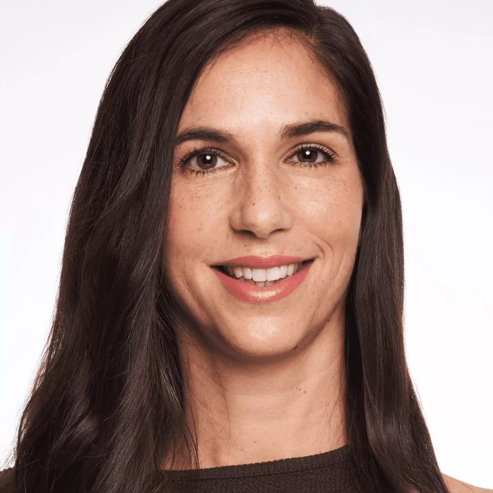 Close-up van een vrouw met lang, donker haar. Ze glimlacht. Ze draagt een subtiele make-up.