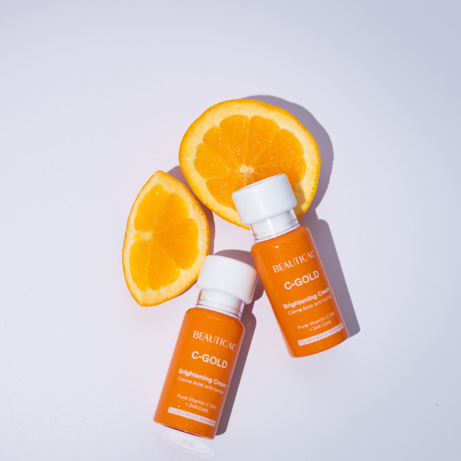 Deux flacons de crème éclaircissante BEAUTICAL C-GOLD avec des tranches d'orange. Flacons orange à bouchon blanc.