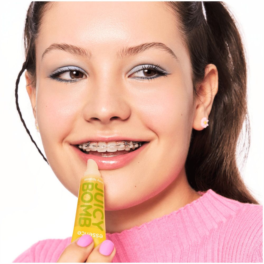Fille avec appareil dentaire, tenant un gloss jaune. Inscription "JUICY BOMB".