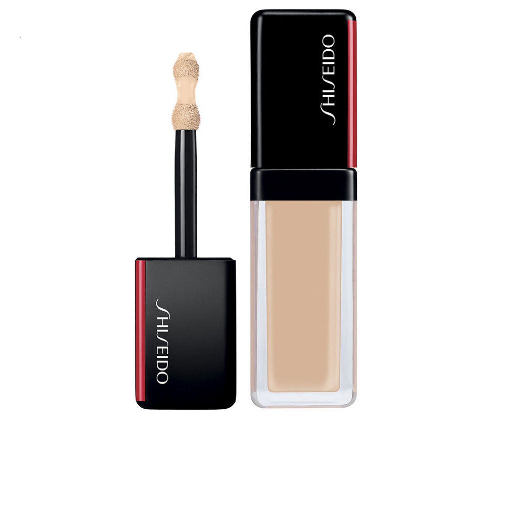 Flacon de correcteur avec applicateur. Capuchon noir avec accent rouge. Inscription Shiseido. Texture beige clair.