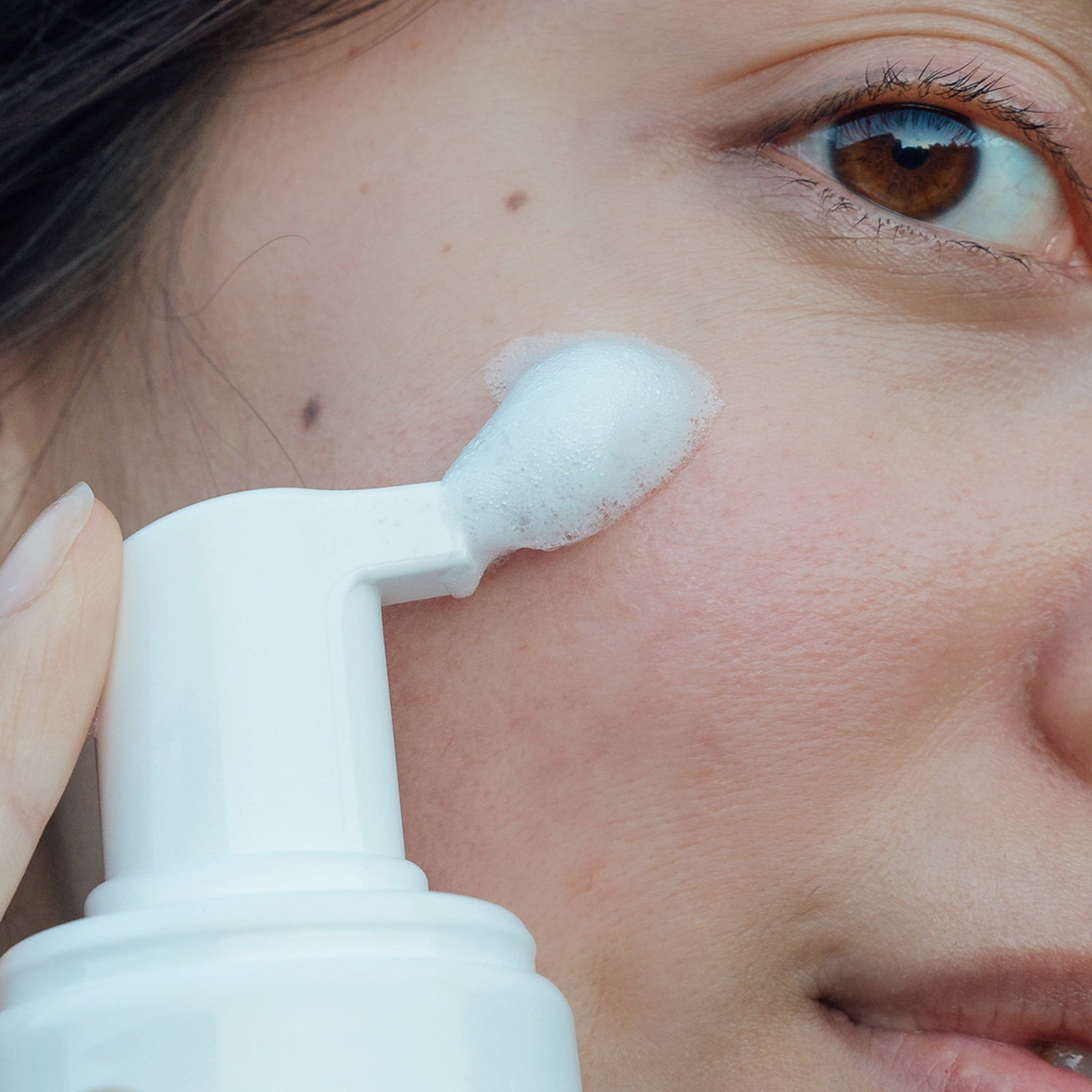 Distributeur blanc appliquant de la mousse sur la peau. Gros plan sur un visage.