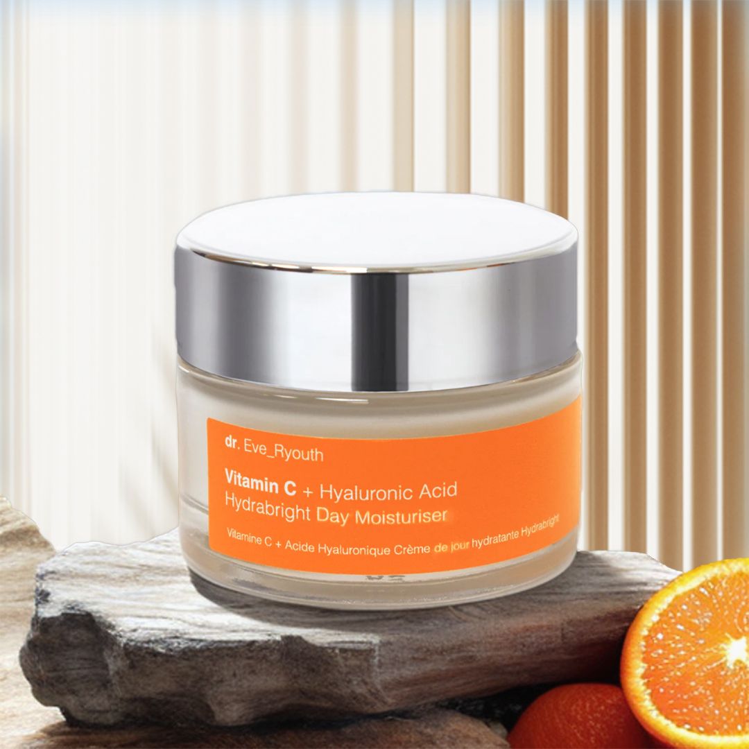 Pot de crème avec couvercle argenté. Inscription: Vitamin C + Hyaluronic Acid Hydrabright Day Moisturiser. Sur pierre et orange.