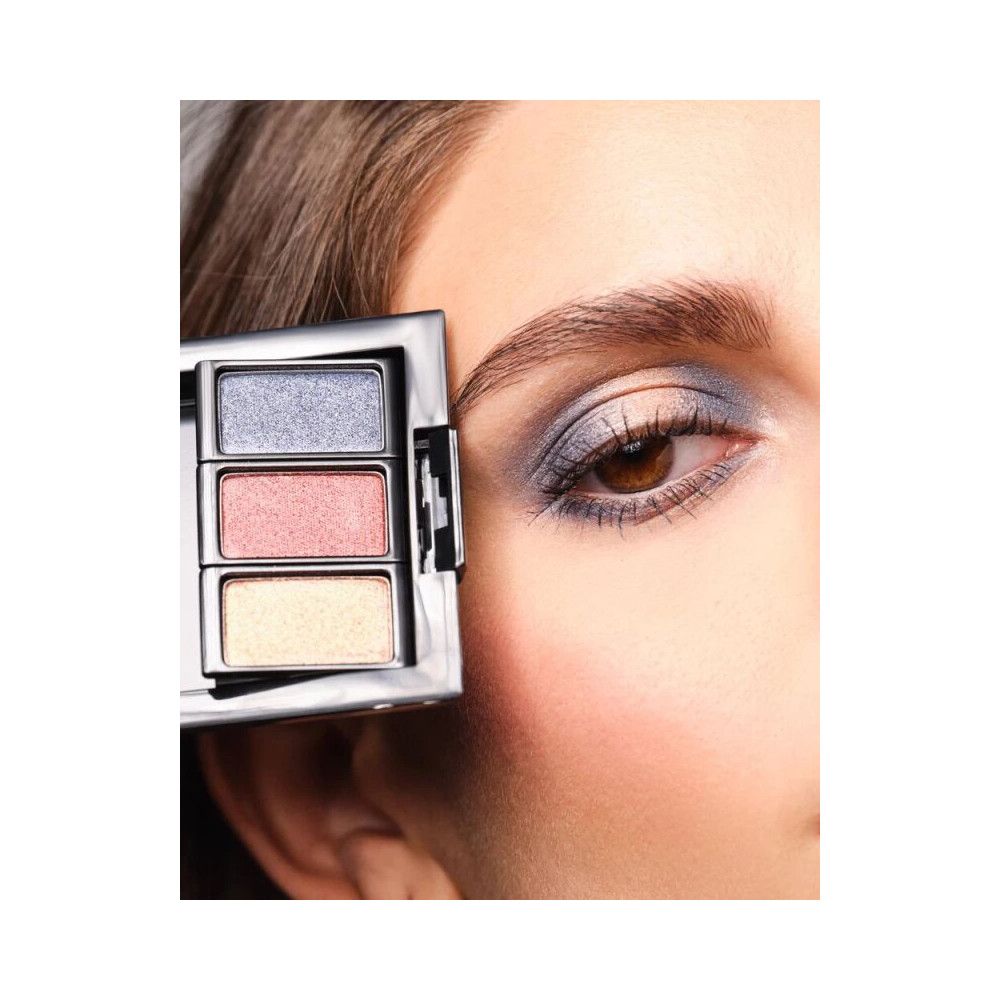 Un trio d'ombres à paupières dans un boîtier argenté. Trois couleurs : bleu, rose et jaune. Appliqué sur un œil.