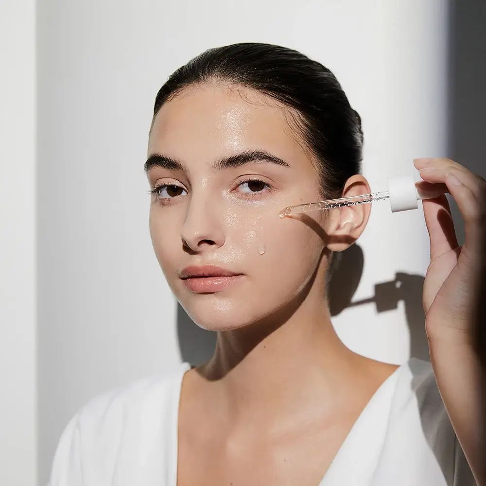 Femme appliquant un produit pour la peau. Pipette avec liquide. Nom du produit non visible.