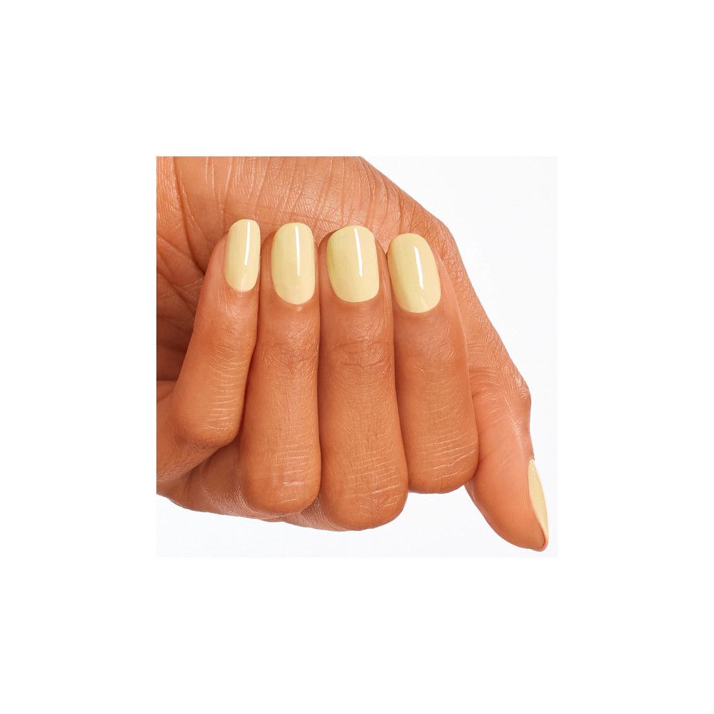Main avec ongles vernis jaune clair. Quatre ongles sont clairement visibles, un légèrement caché.