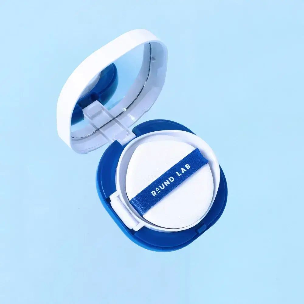Round Lab zonnebrandkussen, geopend. Wit sponsje met blauw lint met logo, in de blauwe en witte verpakking.