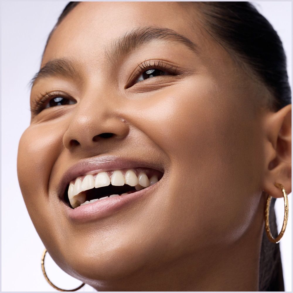 Portrait d'une femme souriante. Elle porte des créoles dorées. Ses dents sont visibles.