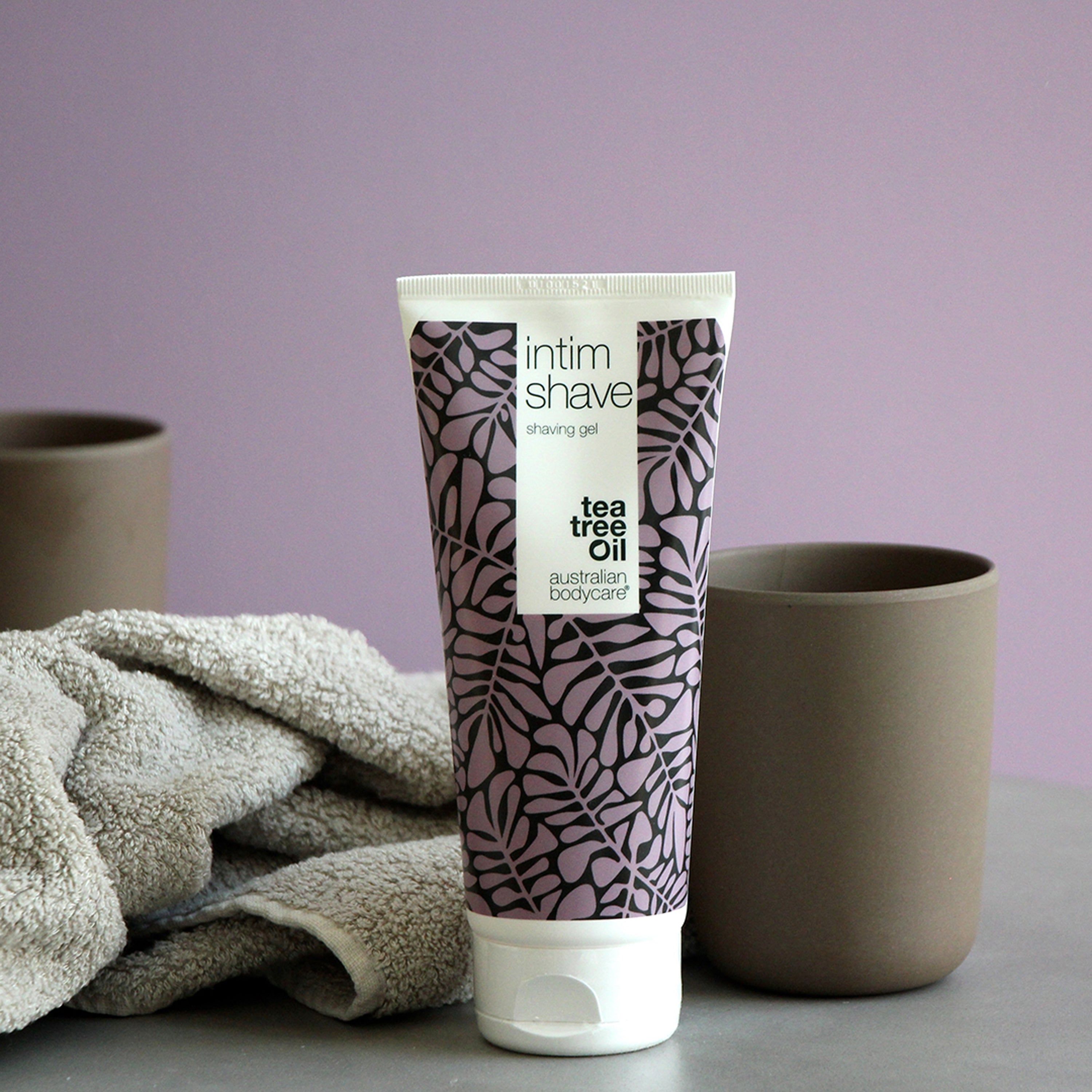 Tube de gel à raser Intim Shave, à côté de tasses et d'une serviette. Texte: Tea Tree Oil, Australian Bodycare.