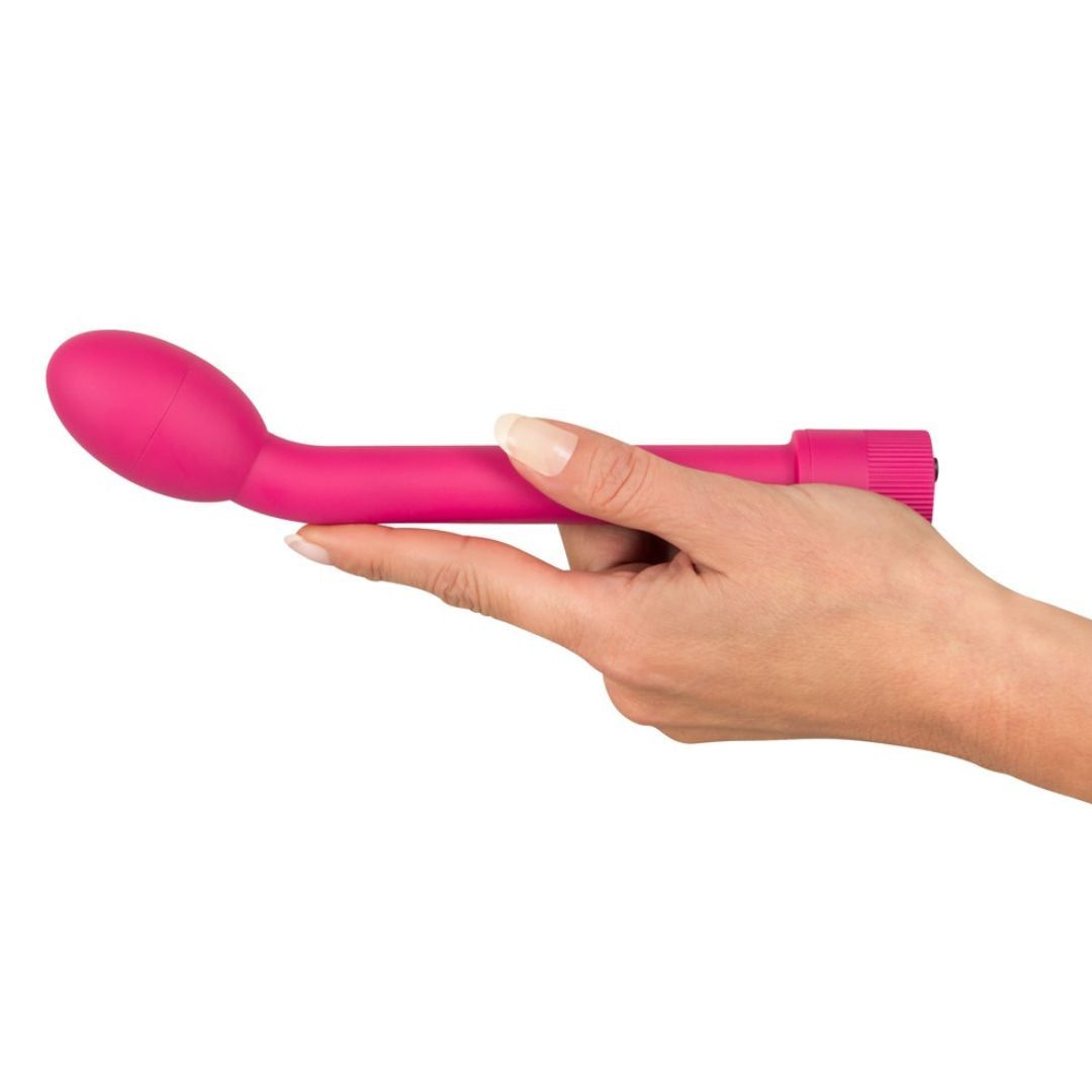 Vibrateur rose tenu par une main. Tête ovale, tige incurvée, base cannelée.