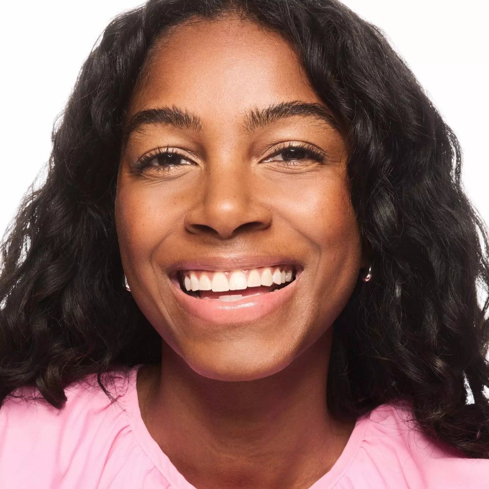 Portret van een lachende vrouw met donker haar. Ze draagt een roze top.