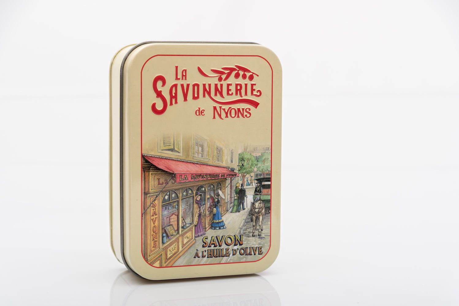 Gesloten rechthoekige metalen doos. Opschrift: La Savonnerie de Nyons. Illustratie van een boetiek. Opschrift: Savon à l'huile d'olive.