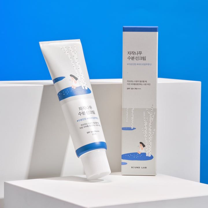 Tube et boîte blancs avec accent bleu. Illustration d'une personne au bord d'un lac. Texte coréen. SPF 50+ PA++++.