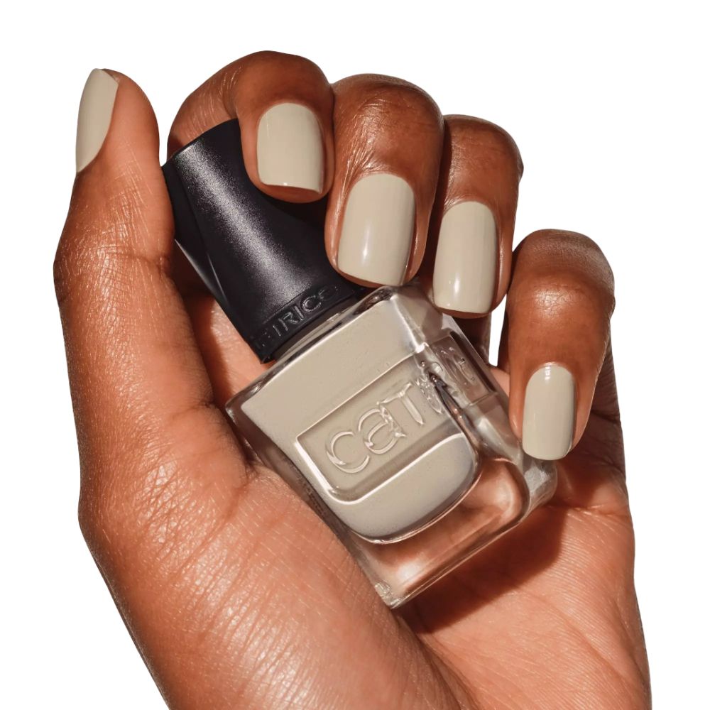 Main avec ongles vernis et flacon de vernis à ongles. Vernis crème. Marque Catrice.