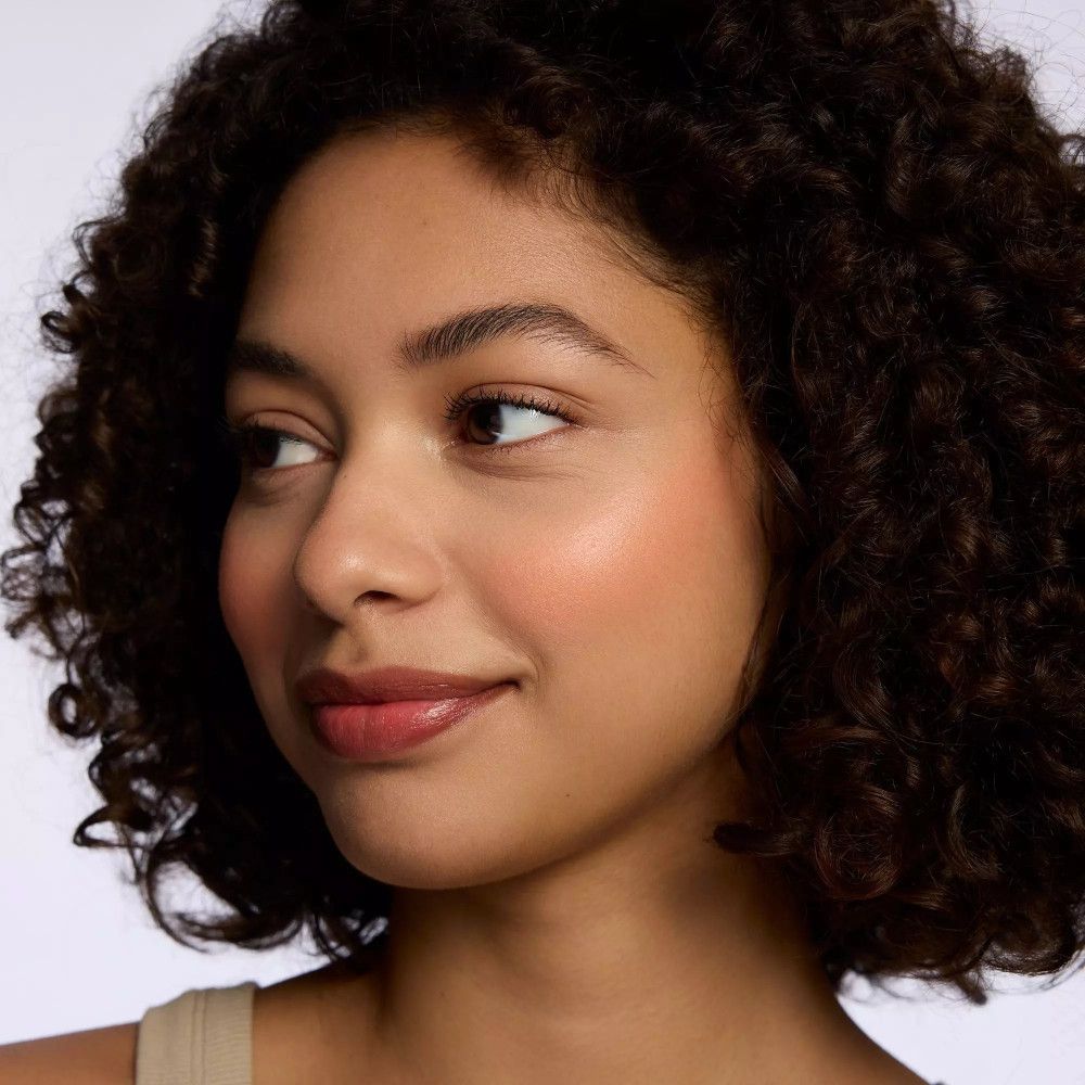 Femme aux cheveux bouclés et blush sur les joues. Elle regarde sur le côté.