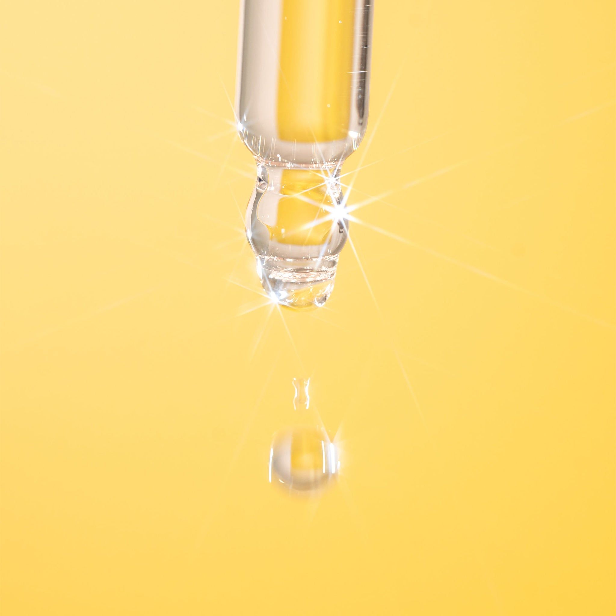 Close-up van een pipet met een druppel vloeistof. Gele achtergrond. Vloeistof druppelt uit de pipet.