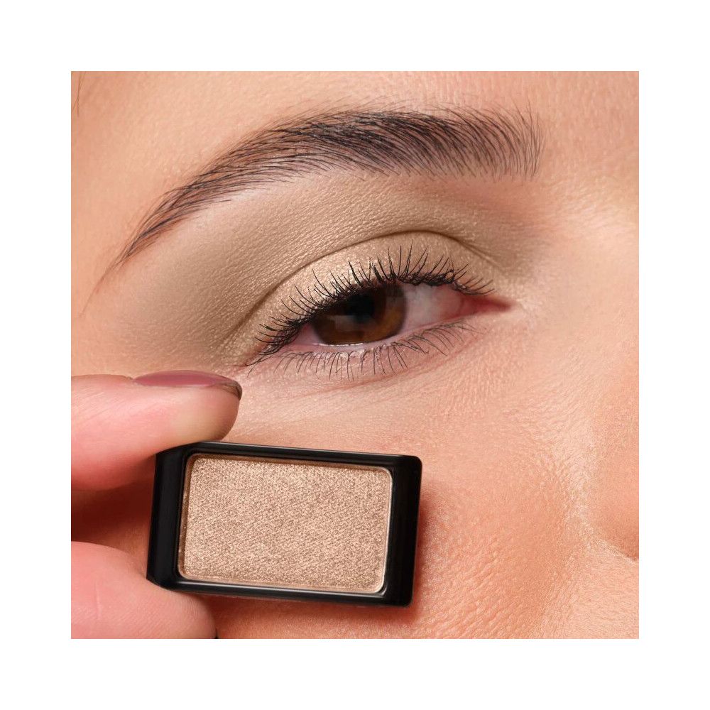 Un fard à paupières unique dans un boîtier noir. Le fard à paupières est brun clair et est tenu devant un œil.